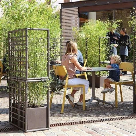 Commercial planters with privacy screens and greenery defining an outdoor restaurant seating area